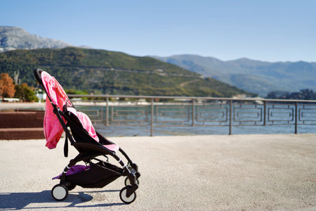 Baby stroller stands on the coast of the sea against the backdrop of mountains
