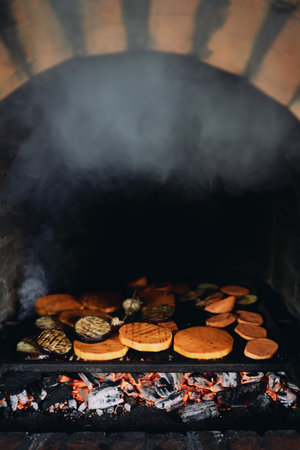 Sliced fresh vegetables are baked on a grill in a brick oven