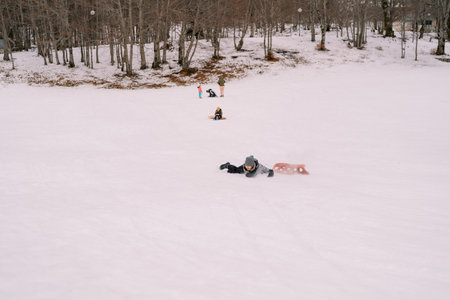 Young woman fell off the sled and lies on her stomach in the snow, looking awayの写真素材