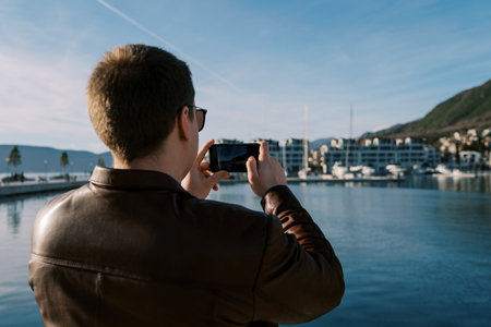 Man takes pictures of high-rise buildings on the seashore with a smartphone. Back viewの写真素材