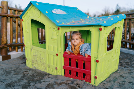 Little girl looks out the window of a toy house on the playgroundの写真素材
