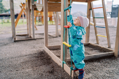 Little girl is trying to reach the top rung of a rope ladder by standing on her tiptoes