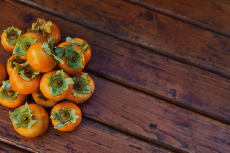 Pile of orange persimmons lies on a wooden table. Top view. Croppedの写真素材