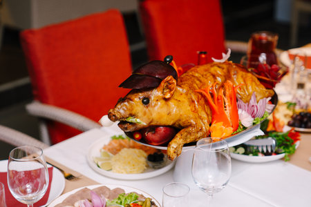 Roasted little pig lies on a platter in a restaurant next to snacks