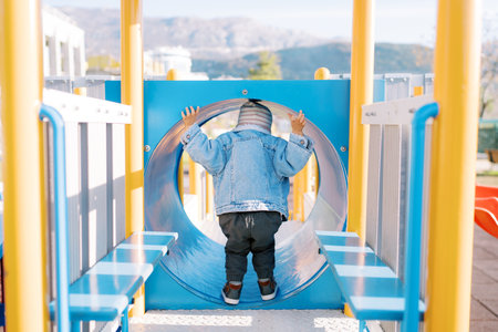 Little girl stands in a pipe on a slide and looks into it. Back view
