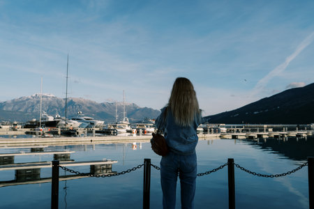 Woman stands on a pier by the sea and looks at the moored yachts. Back viewの写真素材