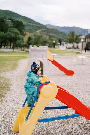 Little girl climbs the stairs to the colorful slide in the playground. Side viewの写真素材