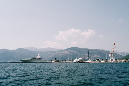 Expensive yachts stand at the pier with a port crane against the backdrop of a mountain rangeの写真素材