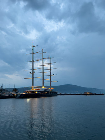 Illuminated sailing yacht stands at the pier against the backdrop of dusk