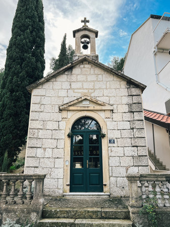 Dubrovnik, Croatia - 25 december 2022: Bell with a cross over an old stone chapel with a green...