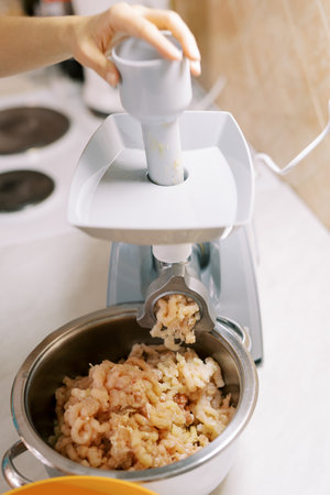 Housewife makes minced meat on an electric meat grinder