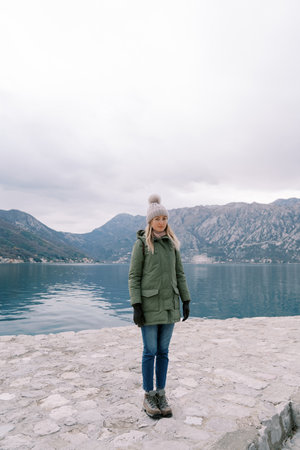 Young woman stands on a pier near the sea against the backdrop of mountainsの写真素材