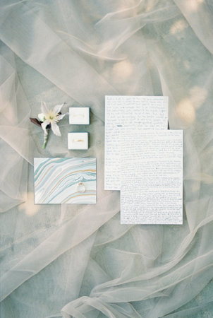 Wedding rings in boxes lie on the veil near the boutonniere and vows of the bride and groomの写真素材
