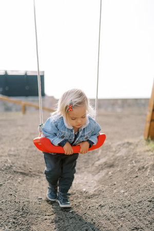 Little girl lies on her stomach on a swing, holding on to it with her handsの写真素材