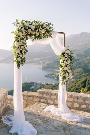 Wedding arch decorated with white roses stands on an observation deck above the sea and a mountainous coastの写真素材