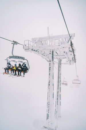 Four-seater chairlift carrying tourists on skis climbs up the misty mountain
