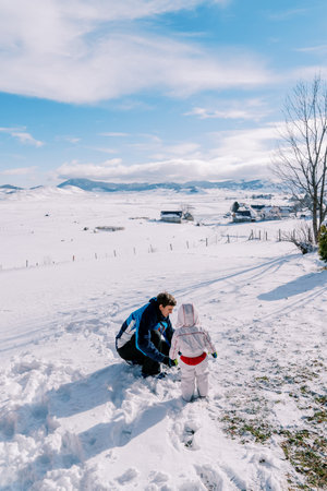 Small child stands next to his father, who is squatting in the snow, and looks at him. Back viewの写真素材