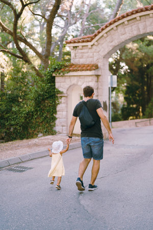 Dad and a little girl run holding hands along the road to the park. Back viewの写真素材