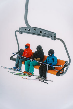 Skiers in ski suits and helmets ride on a chairlift to a foggy mountainの写真素材
