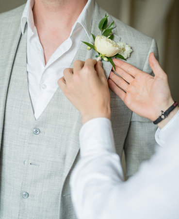 Best man attaches the boutonniere to the lapel of groom jacket. Cropped. Facelessの写真素材