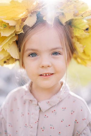 Little surprised girl wearing a crown of yellow leaves. Portraitの写真素材