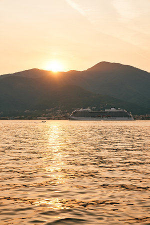 White cruise ship sails on the sea against the backdrop of mountains at sunsetの写真素材