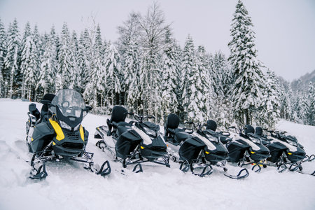 Row of black snowmobiles stands in the snow on a mountain at a ski resortの写真素材