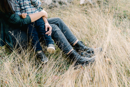 Mom hugs a small child sitting in her arms on a lawn. Cropped. Faceless