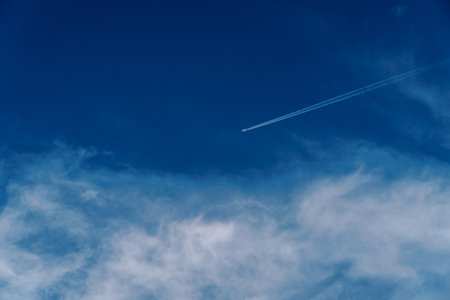 Plane flies in the cloudy sky leaving a trailの写真素材