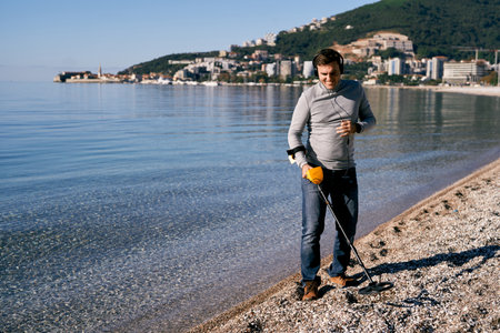 Man in headphones with a metal detector walks along the seashoreの写真素材