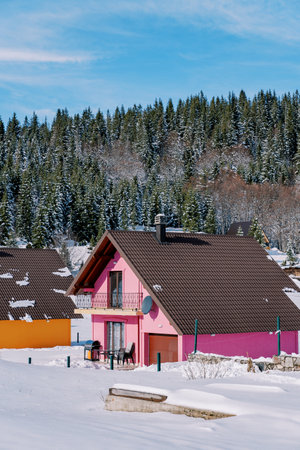 Pink two-story house with a terrace in the snow at the edge of a coniferous forest in the villageの写真素材