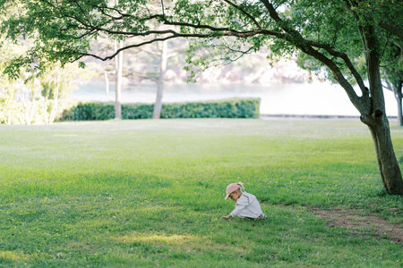 Little girl sits on a green meadow and picks wild flowersの写真素材