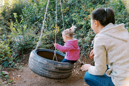 Mom swings a little girl on a tire swing in the forest. Back viewの写真素材