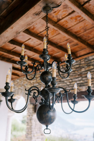 Bronze branched chandelier with spheres and candle bulbs hangs from the wooden ceiling of an ancient villaの写真素材