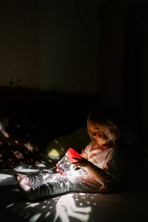 Little girl sits on a bed with a projector night light in her hands and looks at it