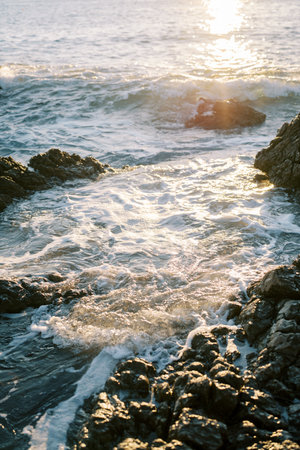 Sea surf rolls onto the coastal rocks in the rays of sunlightの写真素材