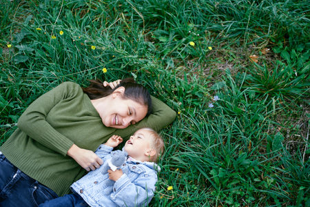 Smiling mother with a little girl lie on a green lawn among colorful wild flowers. Top viewの写真素材