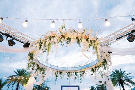 Round stand with spotlights decorated with flowers and white fabric in the light of a garland of light bulbsの写真素材