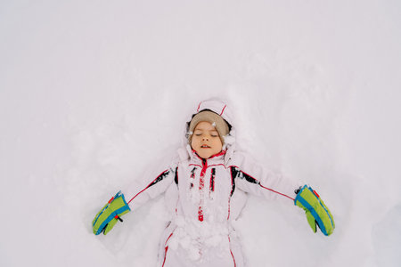 Little girl makes a snow angel lying in a snowdrift with her eyes closed