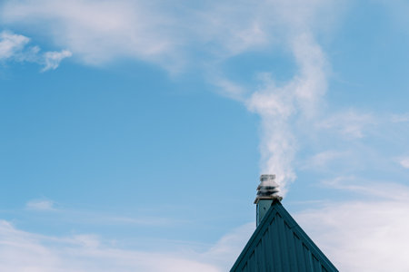 Smoke billows above the chimney of a triangular green corrugated roof of a cottageの写真素材