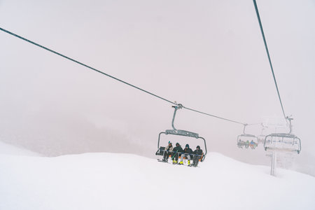 Skiers on chairlift ride up a foggy snowy slopeの写真素材