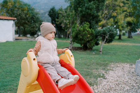 Little girl sits on a colorful slide on the playground and looks into the distanceの写真素材
