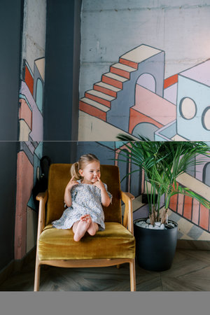 Little smiling girl sitting in a chair near a colorful wallの写真素材