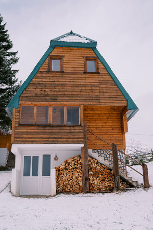 Wooden two-story house with a woodpile under the stairs in a snowy village