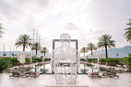 White wire sculpture in the shape of a man stands on the shore of a huge hotel swimming poolの写真素材
