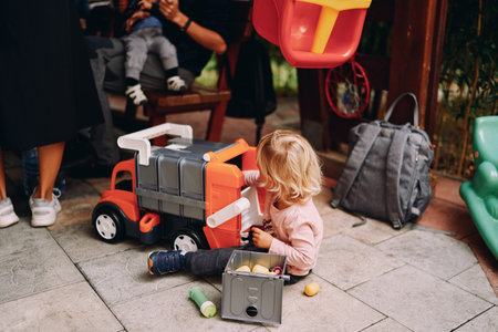 Little girl is playing with a toy car while sitting on the floor. Back viewの写真素材