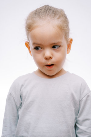 Portrait of a little surprised girl with her mouth open looking to the side on a gray background