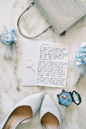 Wedding vow lies on an envelope next to the bride shoes and handbag on a marble table