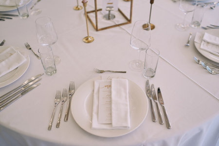 Invitation with a festive menu wrapped in a napkin lies on a plate on a set table