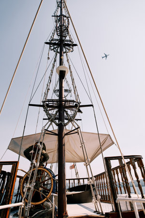 Captain at the helm of a wooden schooner sailing on the sea against the backdrop of an airplane flying in the skyの写真素材